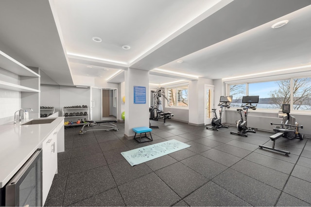exercise room featuring baseboards, beverage cooler, and a sink
