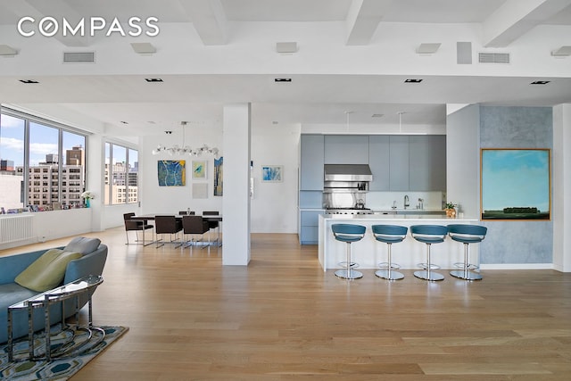 kitchen featuring a breakfast bar area, beam ceiling, wall chimney exhaust hood, open floor plan, and light wood-style flooring