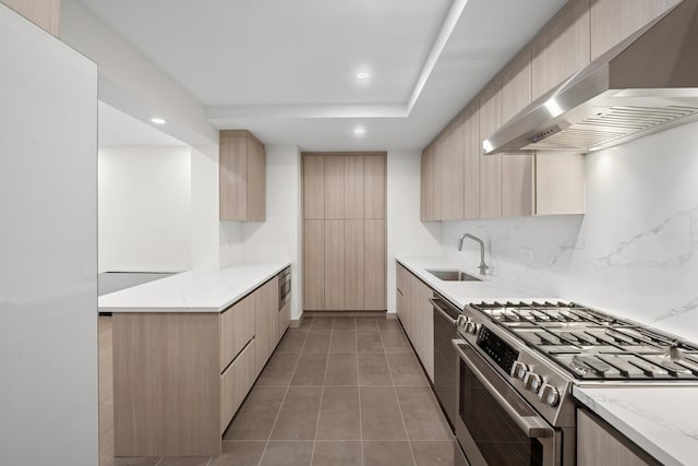 kitchen with wall chimney range hood, light brown cabinetry, a sink, stainless steel appliances, and modern cabinets