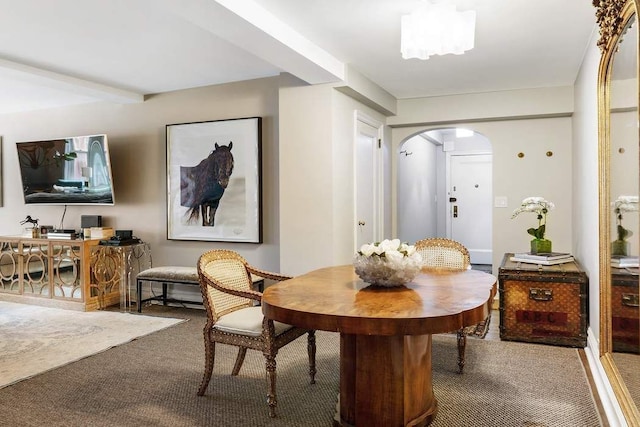 dining space with arched walkways, beamed ceiling, and carpet