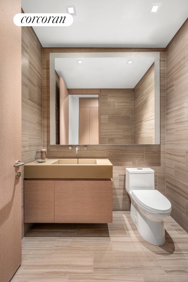 bathroom featuring toilet, tile patterned floors, tile walls, and vanity