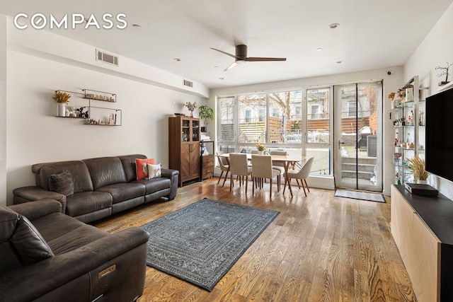living room with a ceiling fan, visible vents, and wood finished floors