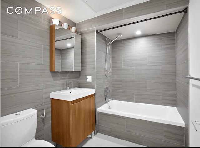bathroom featuring toilet, tiled shower / bath, tile walls, and vanity