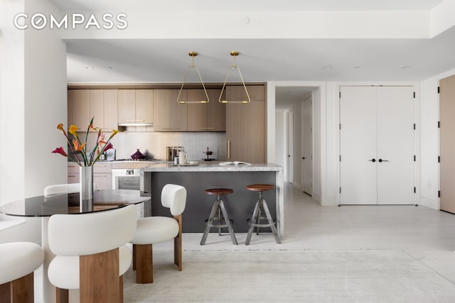 kitchen with a kitchen bar, wall oven, hanging light fixtures, backsplash, and light wood-type flooring