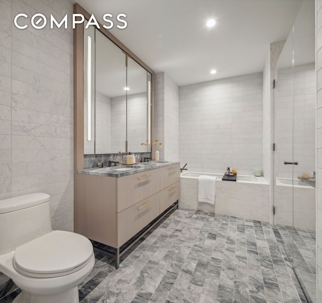 full bath featuring tile walls, toilet, a bath, vanity, and tile patterned floors