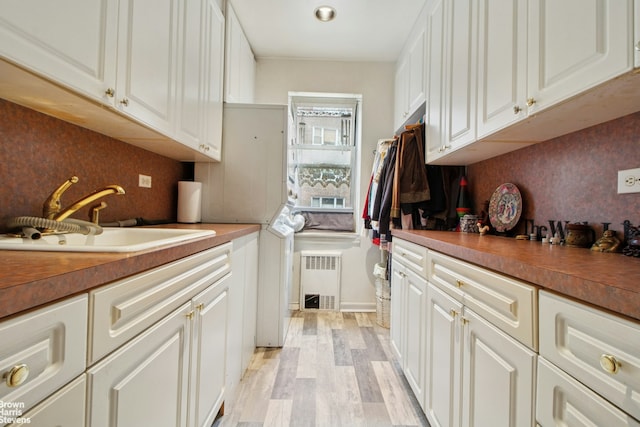 laundry area with light wood finished floors, a sink, cabinet space, stacked washer and clothes dryer, and radiator heating unit