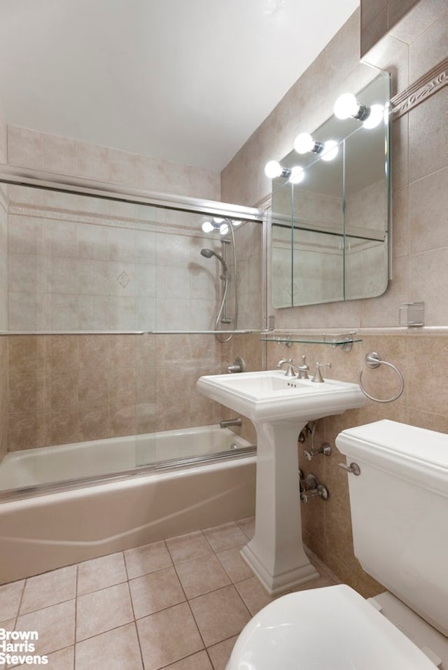 bathroom featuring tile patterned flooring, shower / bath combination with glass door, toilet, and tile walls