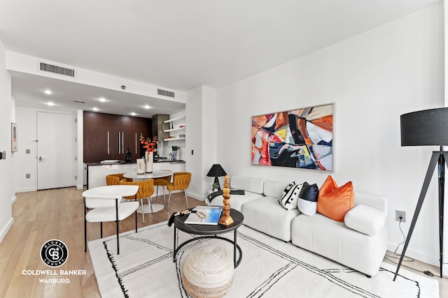 living area with baseboards, light wood-type flooring, and visible vents
