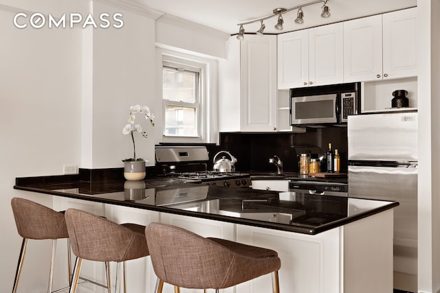 330 E 49th St Unit 9C, New York City, NY 10017 - kitchen with appliances with stainless steel finishes, a peninsula, dark countertops, and white cabinets