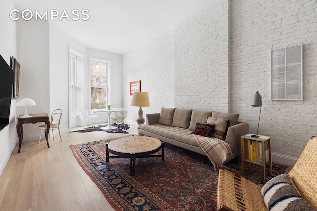 living area with hardwood / wood-style flooring, baseboards, and brick wall