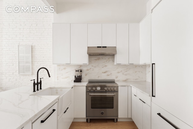 kitchen with high end stainless steel range oven, under cabinet range hood, white cabinets, and light stone countertops