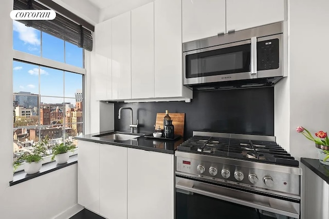 405 W 23rd St Unit 14F, New York City, NY 10011 - kitchen with white cabinets, stainless steel appliances, dark countertops, and a sink
