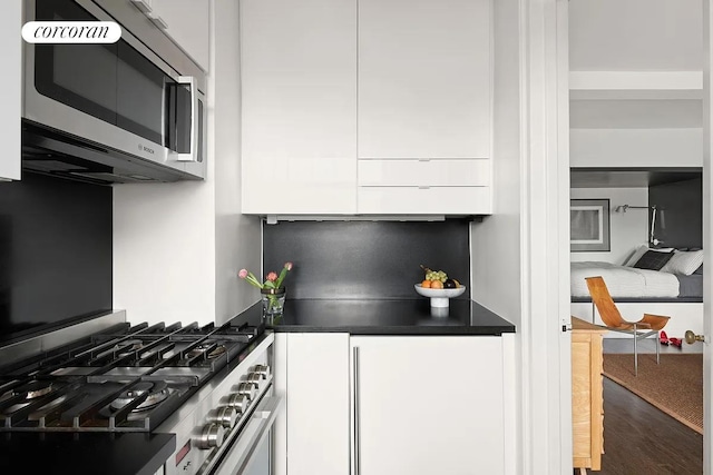 405 W 23rd St Unit 14F, New York City, NY 10011 - kitchen with range, dark countertops, wood finished floors, stainless steel microwave, and white cabinetry