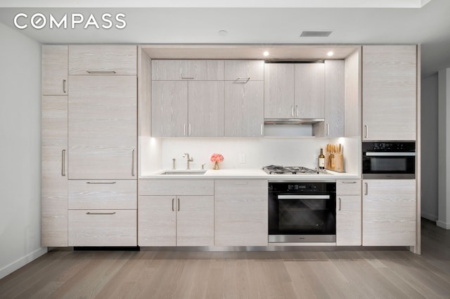 kitchen featuring a sink, wall oven, light wood-style flooring, and oven
