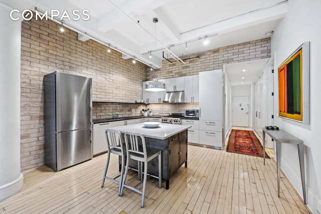kitchen with appliances with stainless steel finishes, track lighting, under cabinet range hood, light wood-style flooring, and white cabinets