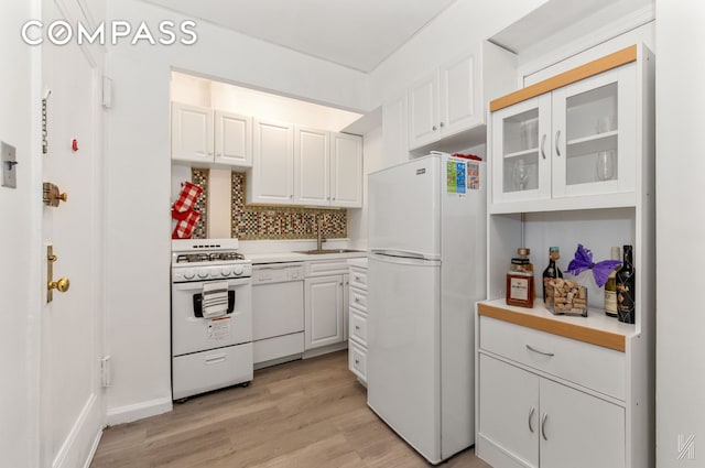 kitchen with white appliances, glass insert cabinets, light countertops, a sink, and light wood finished floors