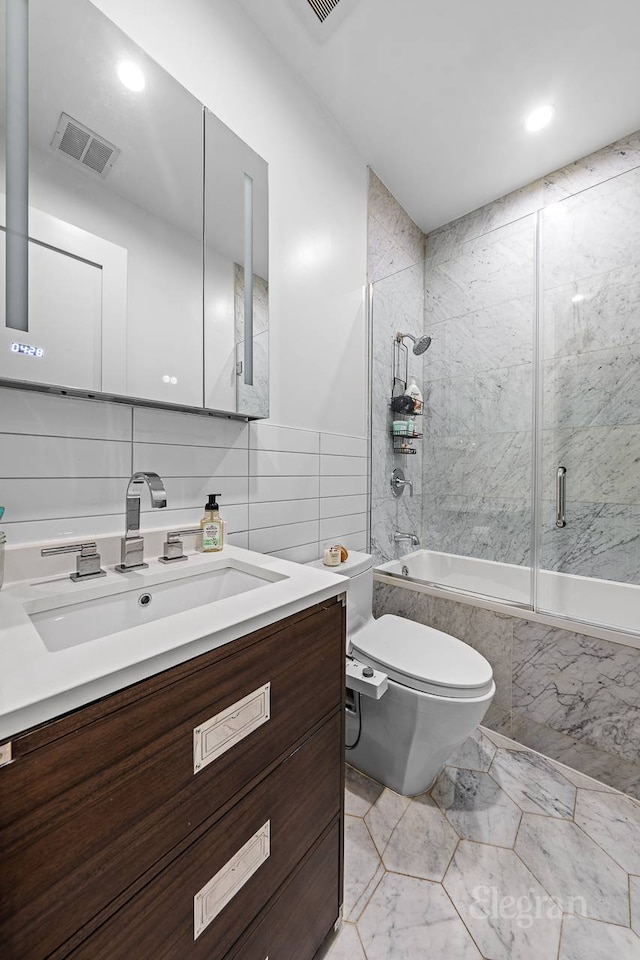 bathroom with vanity, visible vents, toilet, enclosed tub / shower combo, and tile walls