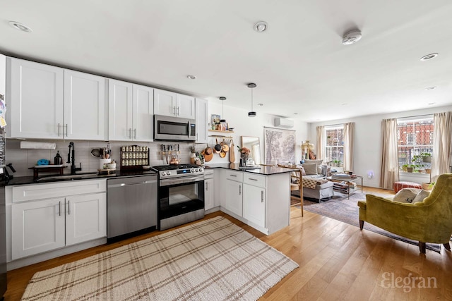 kitchen featuring a peninsula, appliances with stainless steel finishes, a sink, dark countertops, and open floor plan