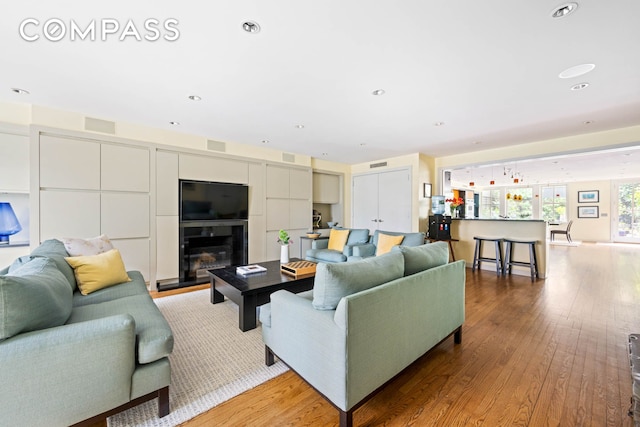 living area with light wood-type flooring, recessed lighting, and a glass covered fireplace