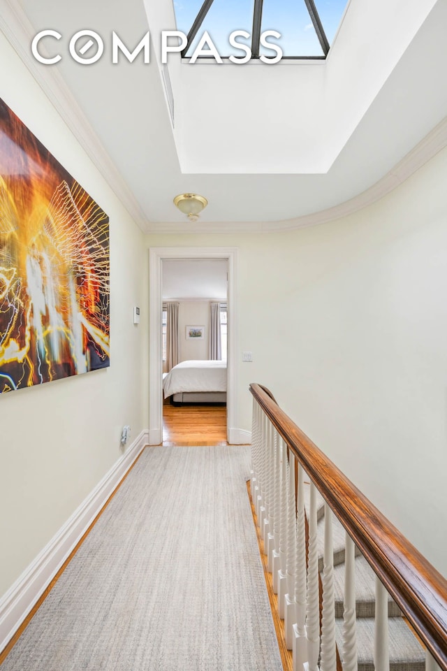 hallway with a skylight, ornamental molding, baseboards, and wood finished floors