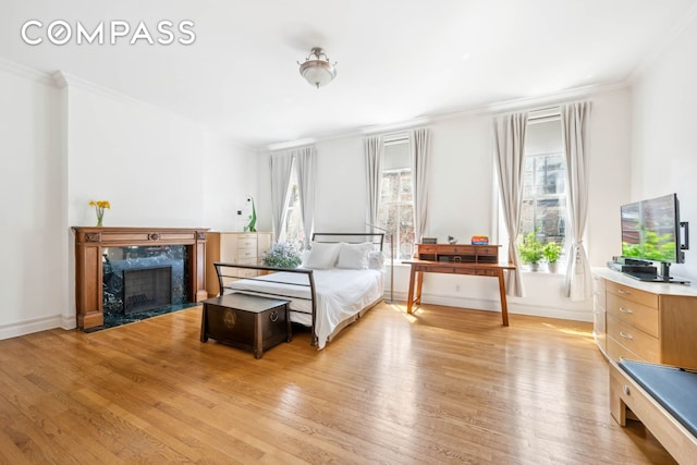 bedroom with light wood-type flooring, ornamental molding, baseboards, and a fireplace