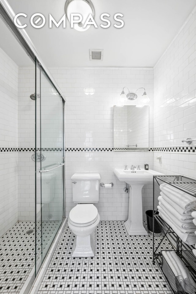 bathroom featuring a shower stall, toilet, tile walls, a sink, and tile patterned floors