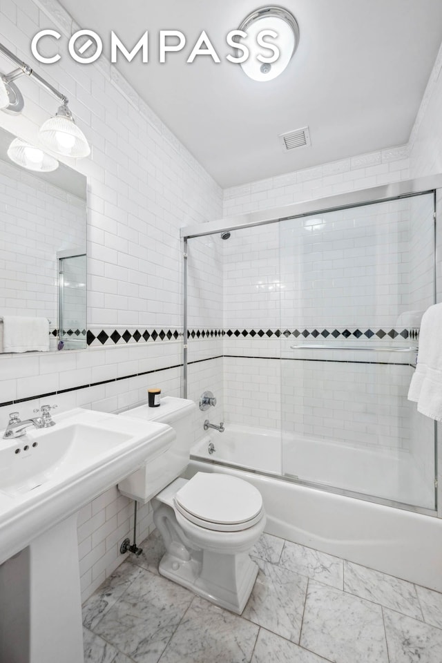 full bathroom with marble look tile flooring, toilet, bath / shower combo with glass door, tile walls, and a sink