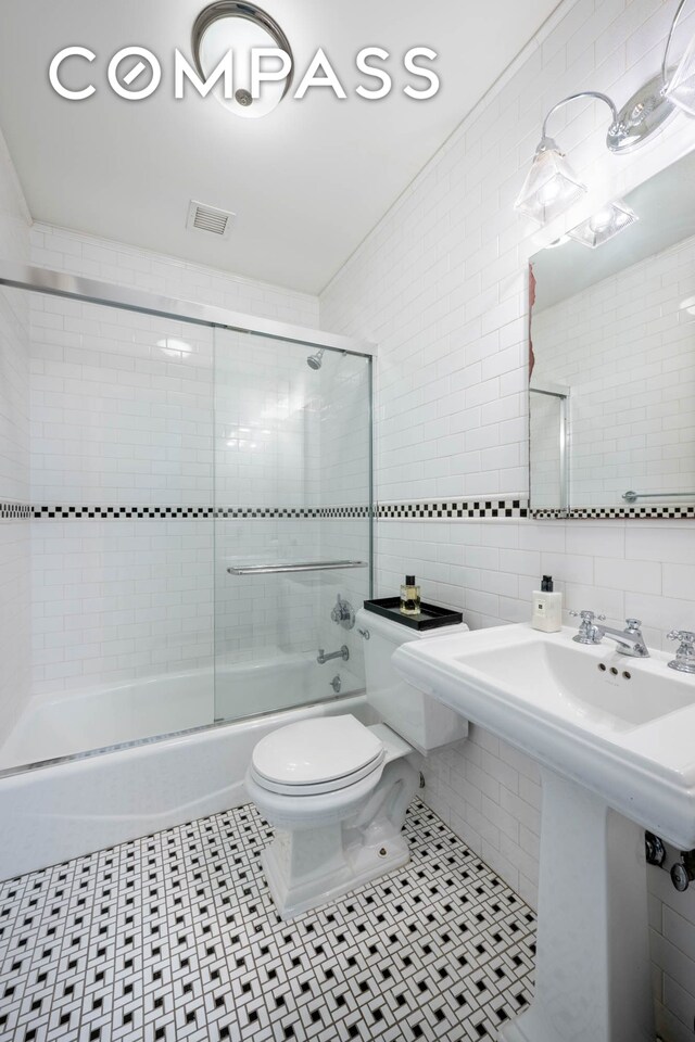 full bathroom with tile walls, toilet, bath / shower combo with glass door, tasteful backsplash, and tile patterned flooring