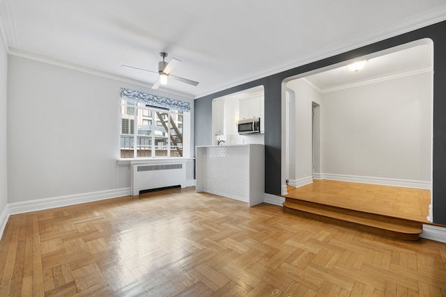 interior space with radiator heating unit, a ceiling fan, baseboards, and ornamental molding