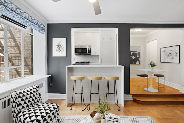 kitchen featuring stainless steel microwave, baseboards, white cabinetry, and a breakfast bar