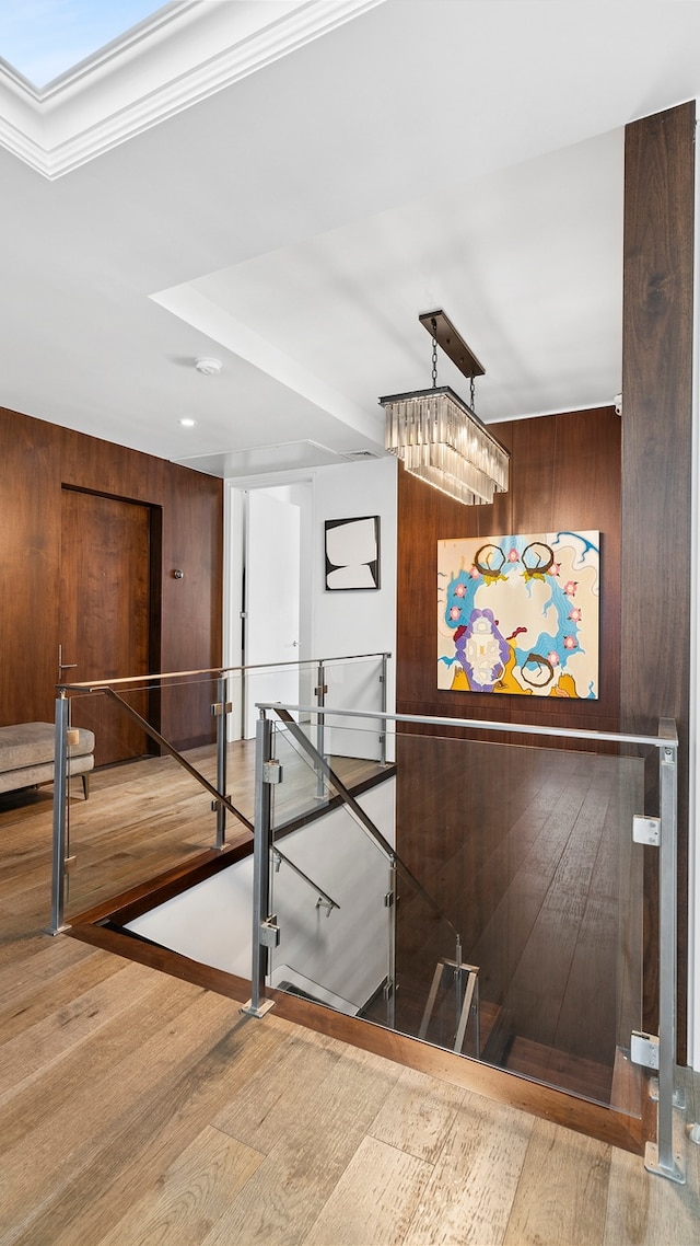 staircase with a chandelier, wood finished floors, and wooden walls