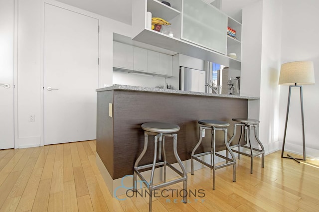kitchen with freestanding refrigerator, white cabinets, light wood-type flooring, a breakfast bar, and a peninsula