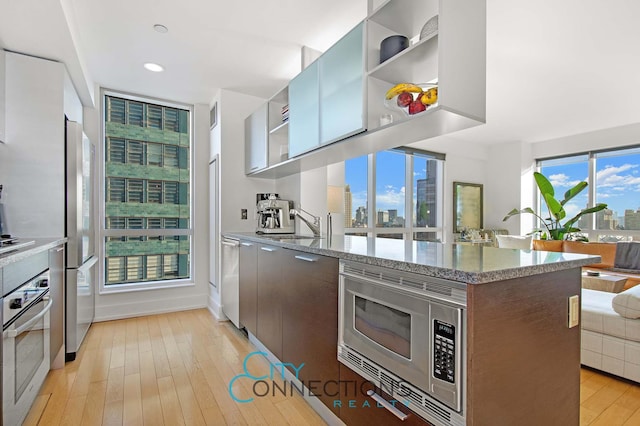 kitchen with open shelves, stainless steel appliances, modern cabinets, light wood-type flooring, and light stone counters