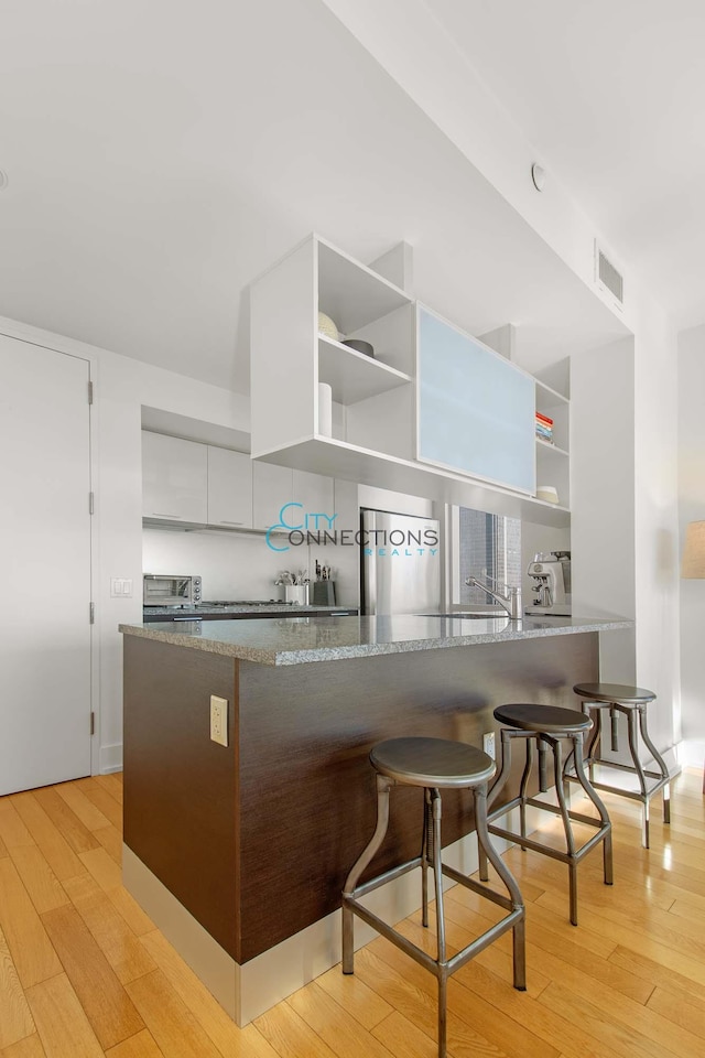 kitchen with open shelves, stainless steel refrigerator, and light wood finished floors
