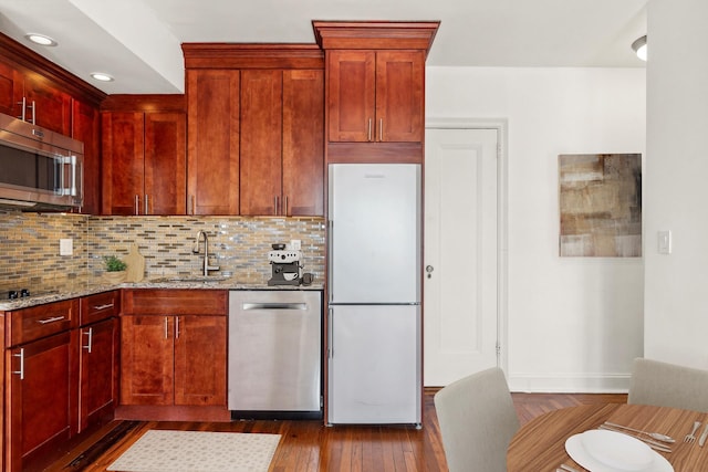 kitchen featuring appliances with stainless steel finishes, a sink, light stone countertops, decorative backsplash, and recessed lighting