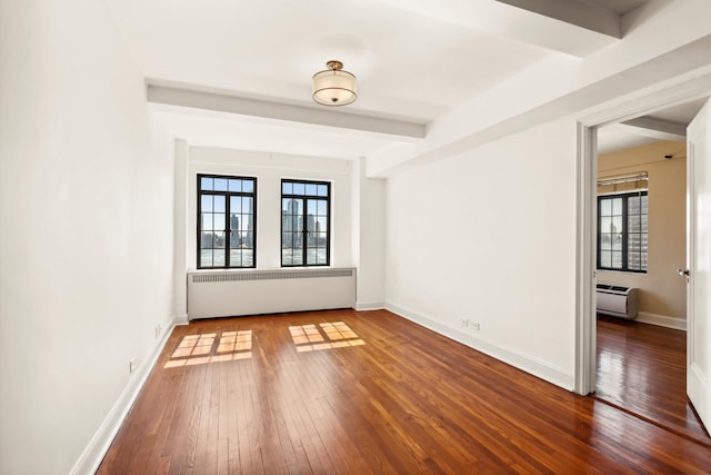 empty room with radiator, plenty of natural light, hardwood / wood-style flooring, baseboards, and beam ceiling