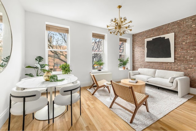 living area featuring a chandelier, light wood finished floors, baseboards, and brick wall