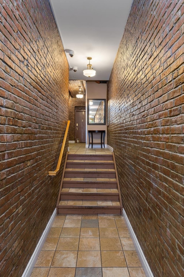 stairway featuring brick wall and baseboards