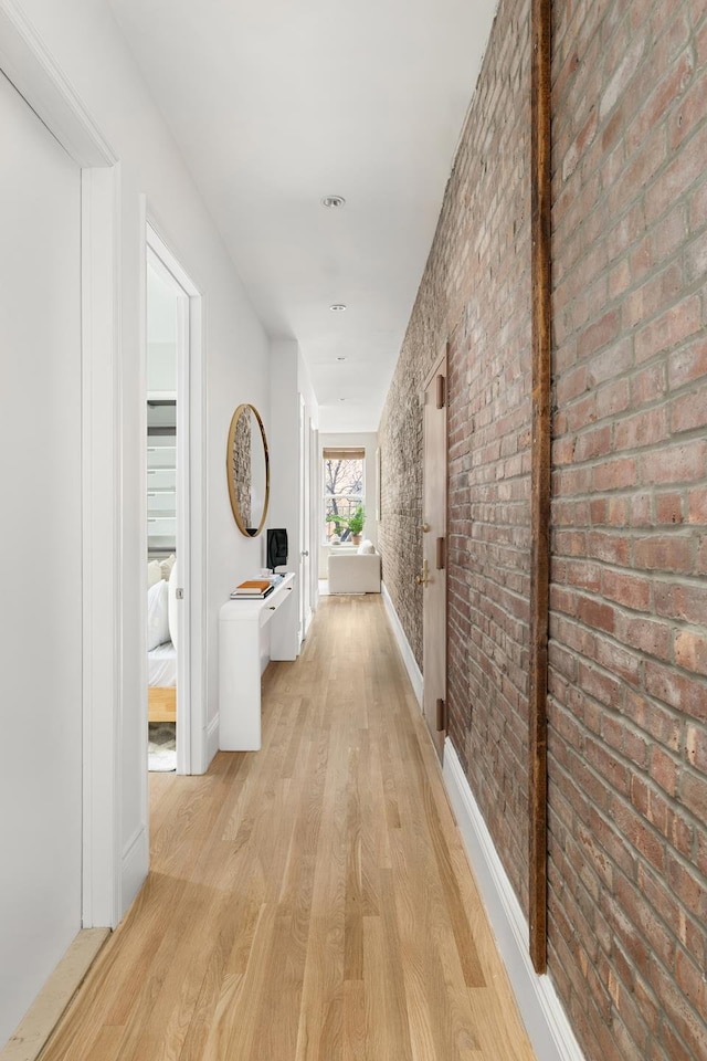 hallway with light wood-style flooring, brick wall, and baseboards