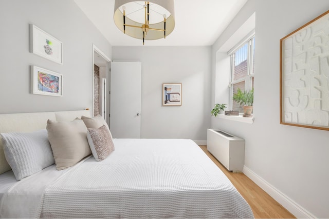 bedroom with light wood finished floors, baseboards, and radiator heating unit