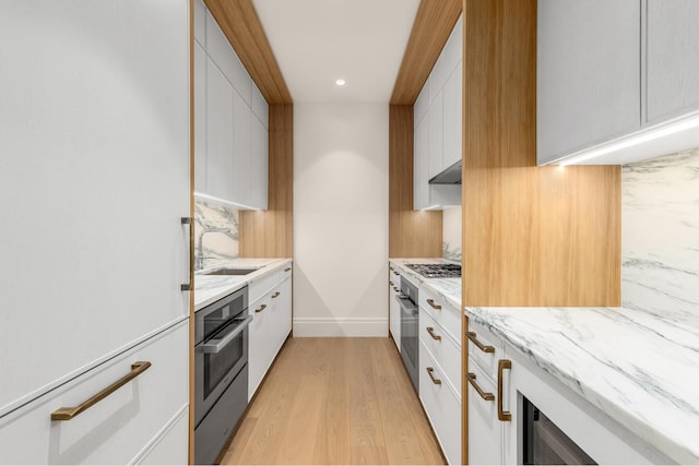 kitchen with light wood finished floors, modern cabinets, a sink, tasteful backsplash, and appliances with stainless steel finishes