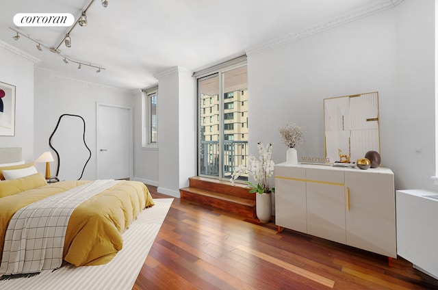 bedroom featuring track lighting, hardwood / wood-style floors, crown molding, and baseboards