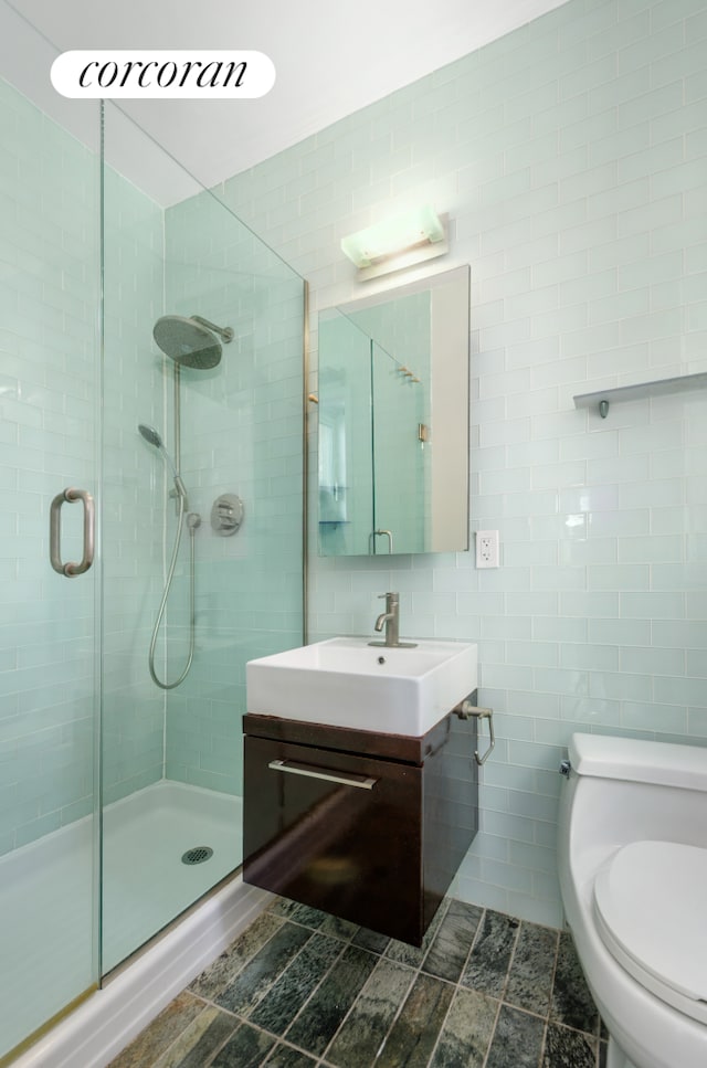 full bath featuring tile walls, a shower stall, vanity, and toilet