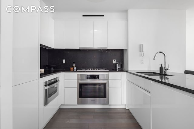 kitchen with oven, a sink, white cabinetry, and exhaust hood