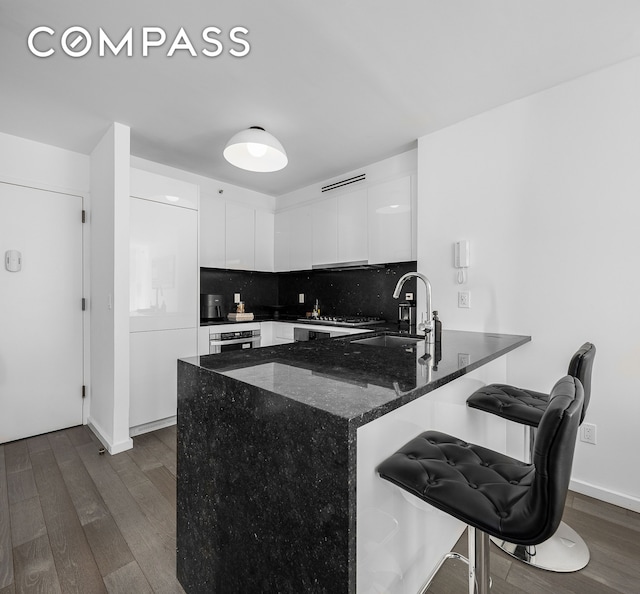 kitchen featuring a peninsula, a sink, white cabinetry, dark wood-style floors, and decorative backsplash