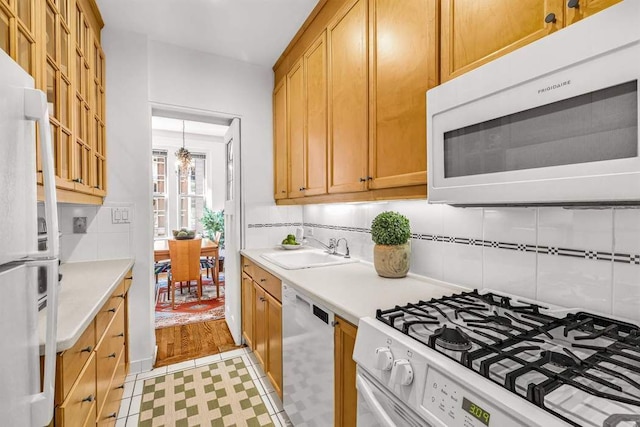 kitchen featuring white appliances, light countertops, a sink, and backsplash