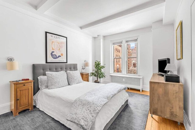 bedroom featuring radiator heating unit, baseboards, beam ceiling, and wood finished floors