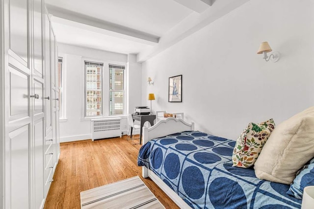 bedroom featuring radiator heating unit, light wood-style flooring, baseboards, and beamed ceiling