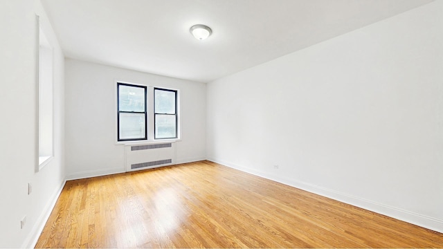 spare room featuring baseboards, radiator heating unit, and light wood-style floors