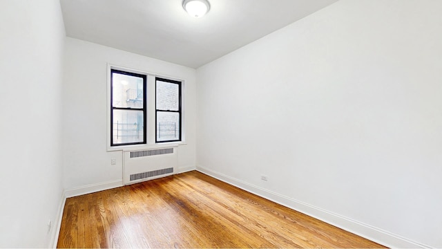 unfurnished room with radiator, baseboards, and light wood finished floors